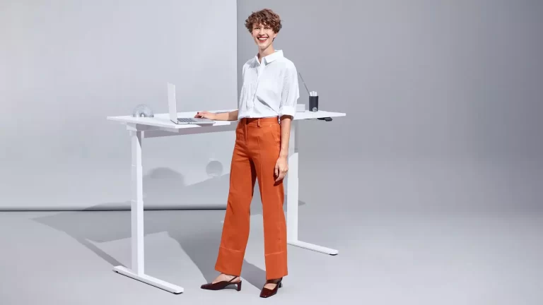 An executive woman standing next to the Level Lift height adjustable desk, designed by Bene and distributed by Walls to Workstations